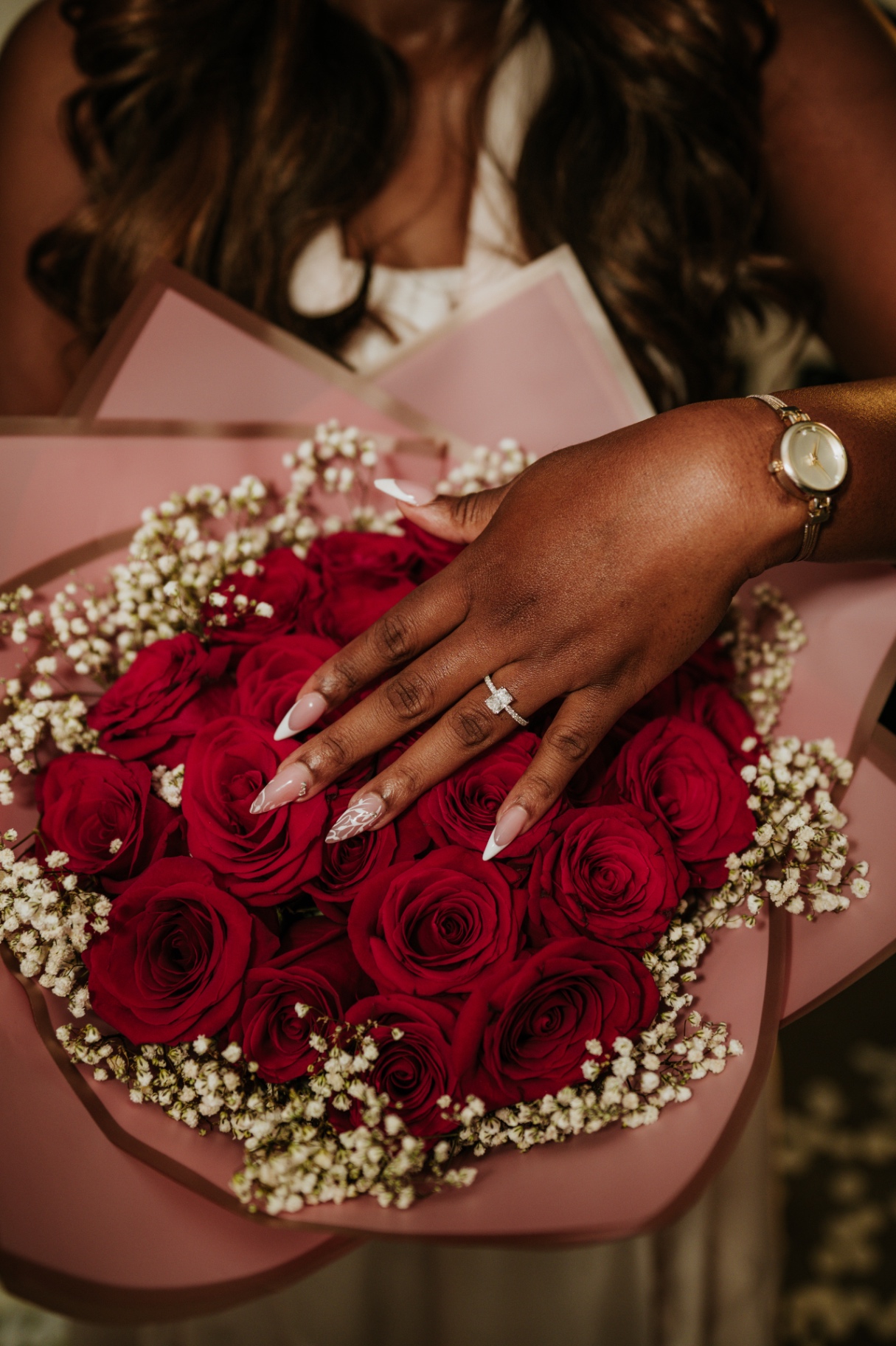 Riziane showing her engagement ring over burgundy roses